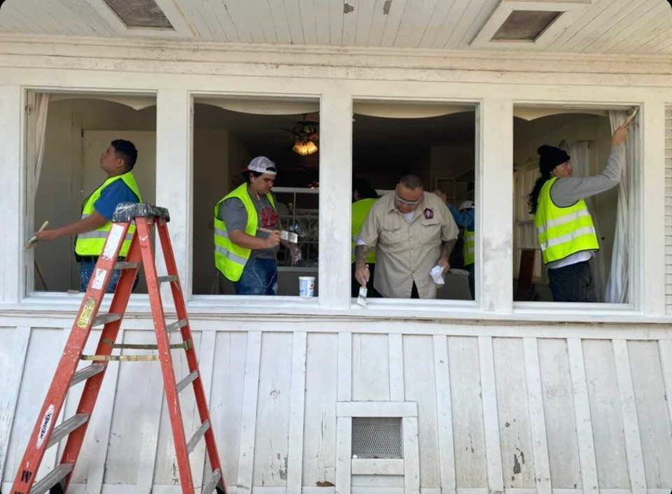 Four tradespeople stand in structure painting open window frames.