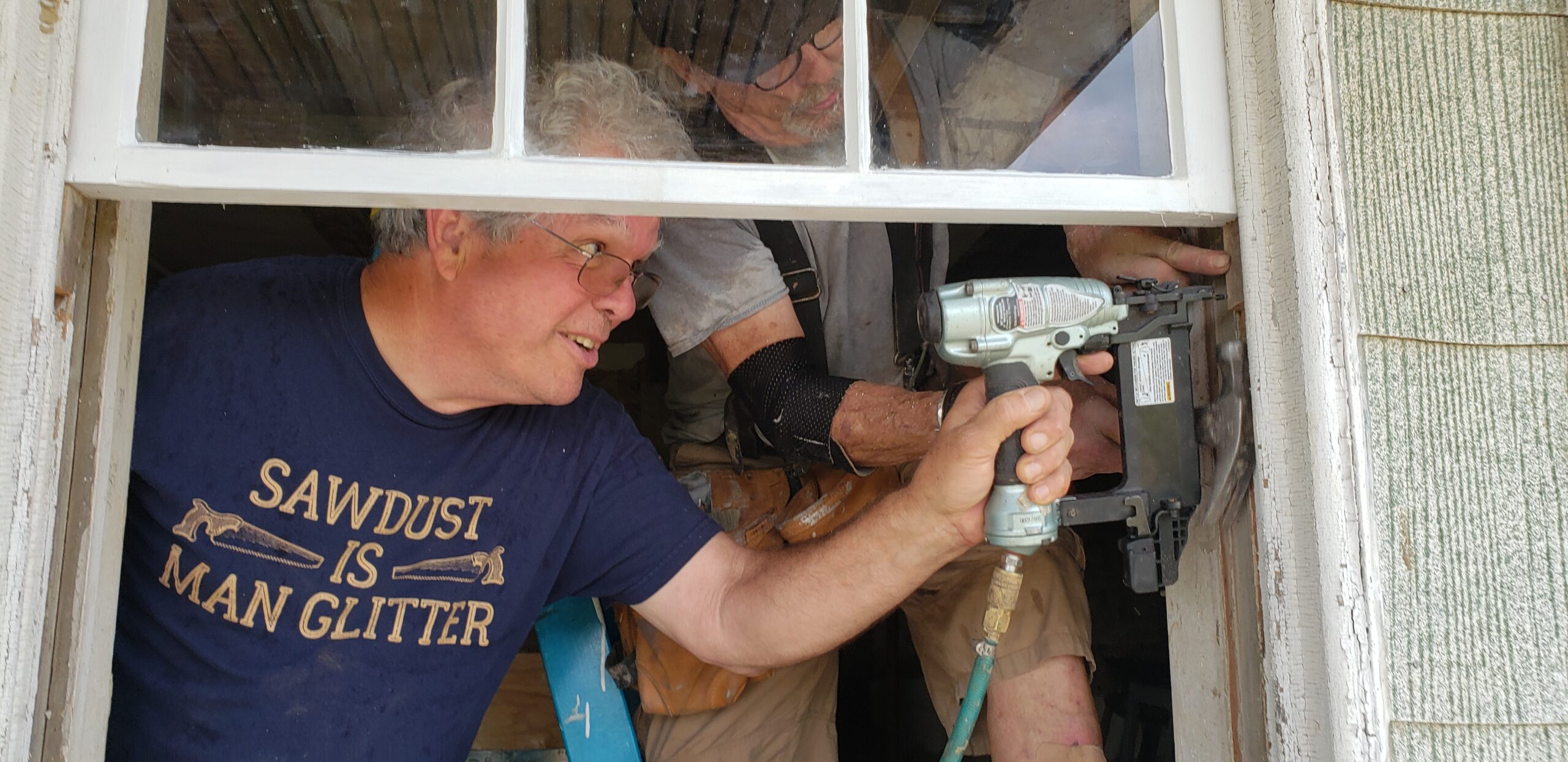 Two men at a window with a power tool