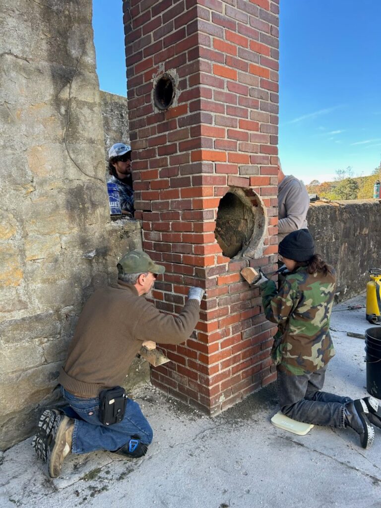Two attendees of the Arthurdale Heritage Masonry workshop repoint brick.
